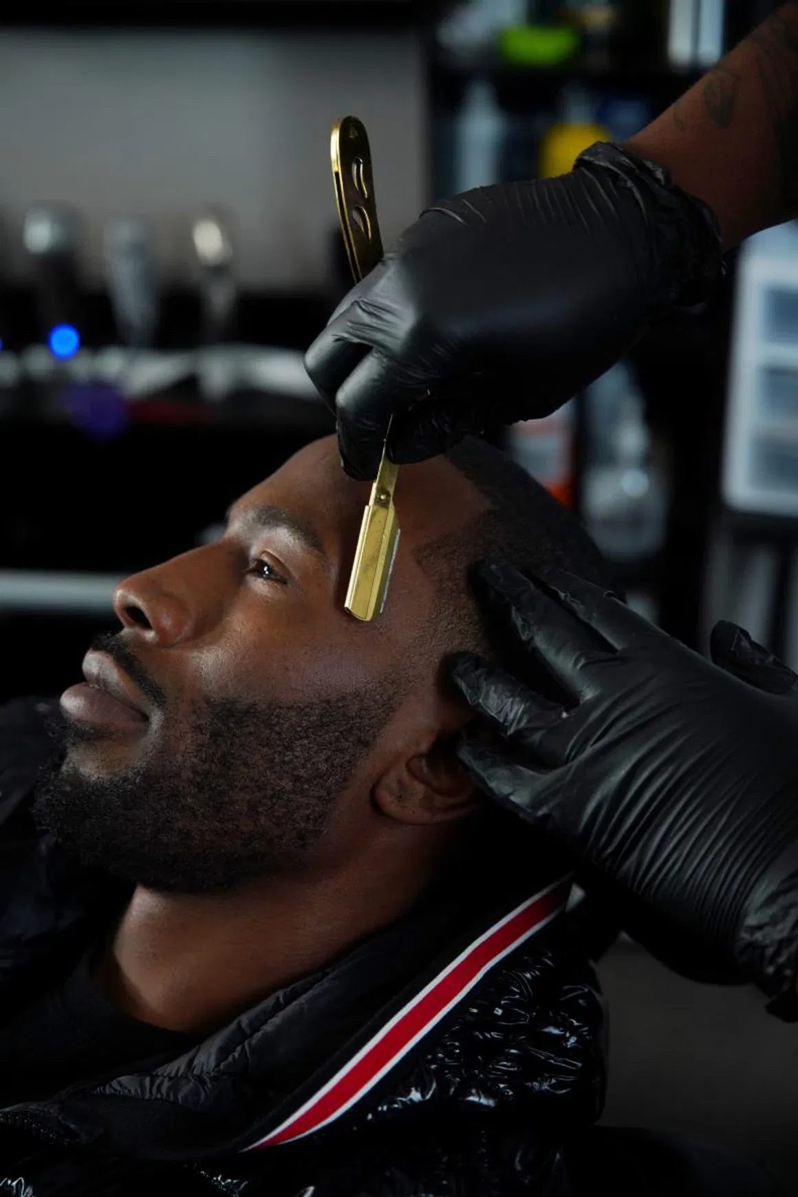 Barber using a gold straight razor to clean up a client's hairline